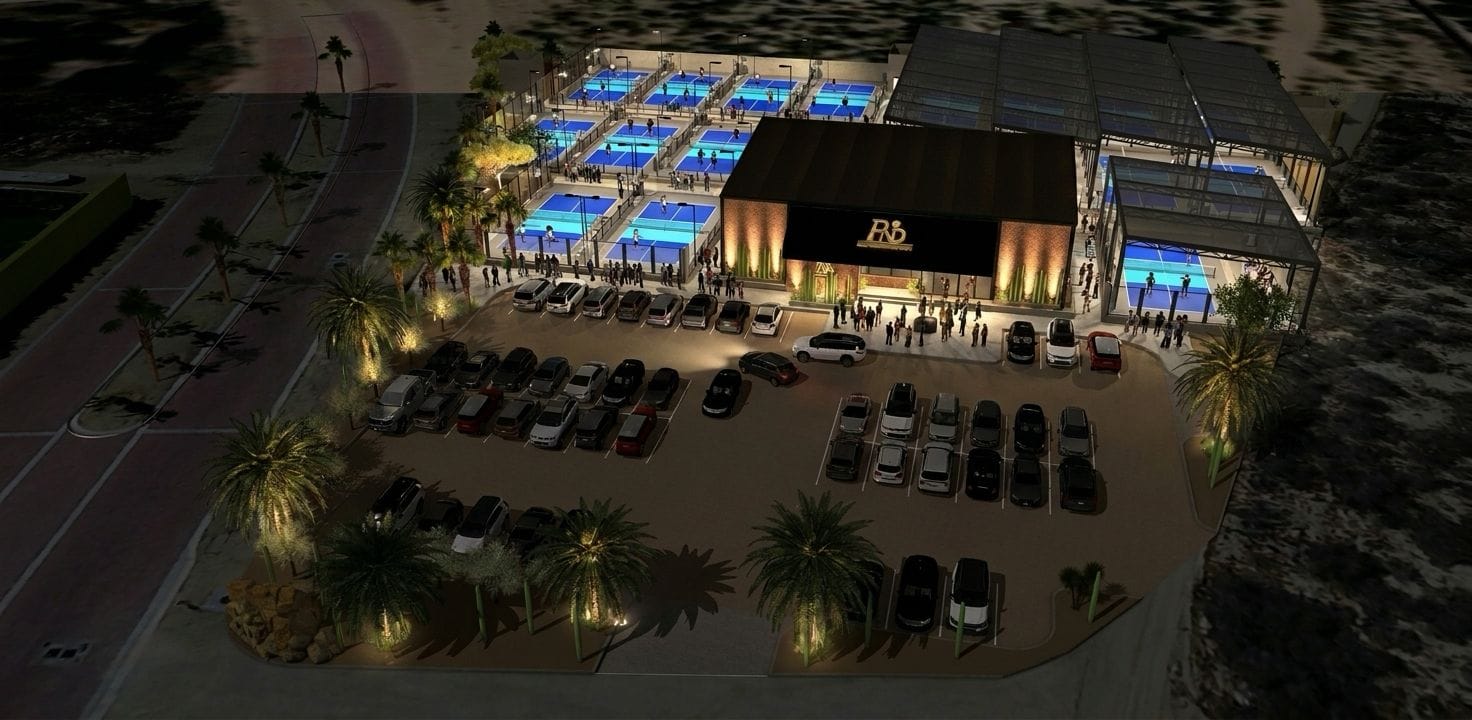 Night aerial of the full facility -- courts and two-story clubhouse aglow